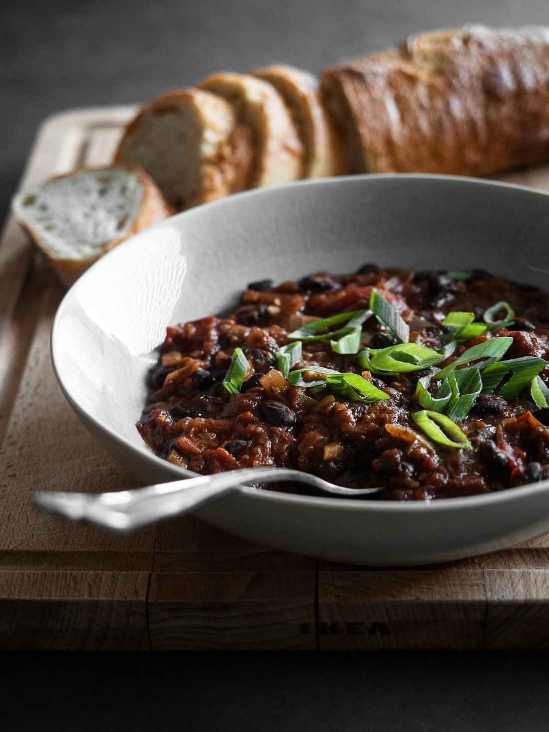 Tigela funda de feijoada com cebolinha, ao lado de pão, sobre tábua de madeira