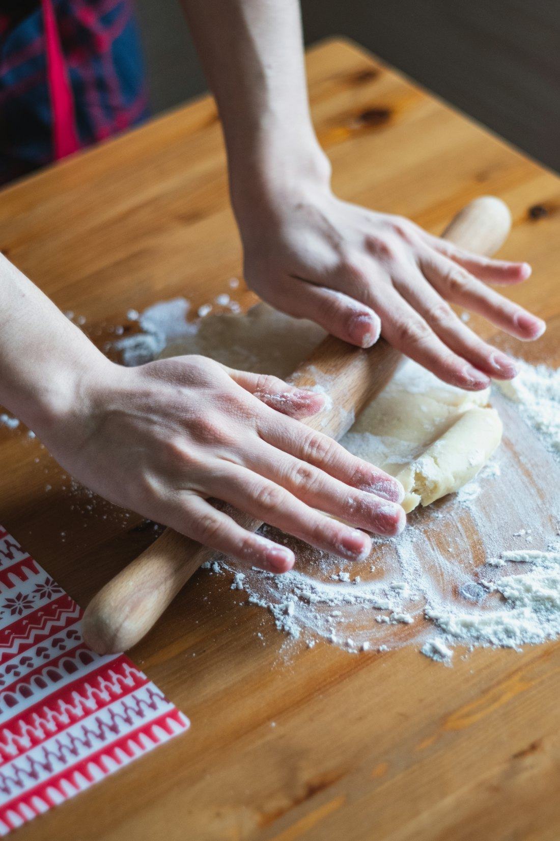 Mãos abrindo massa com rolo sobre mesa enfarinhada